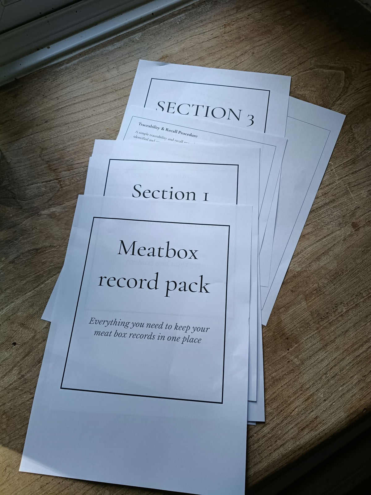 A set of white paper record labels or envelopes labeled 'Meatbox record pack' and 'Section 1', 'Section 2', and 'Section 3' arranged on a wooden surface.