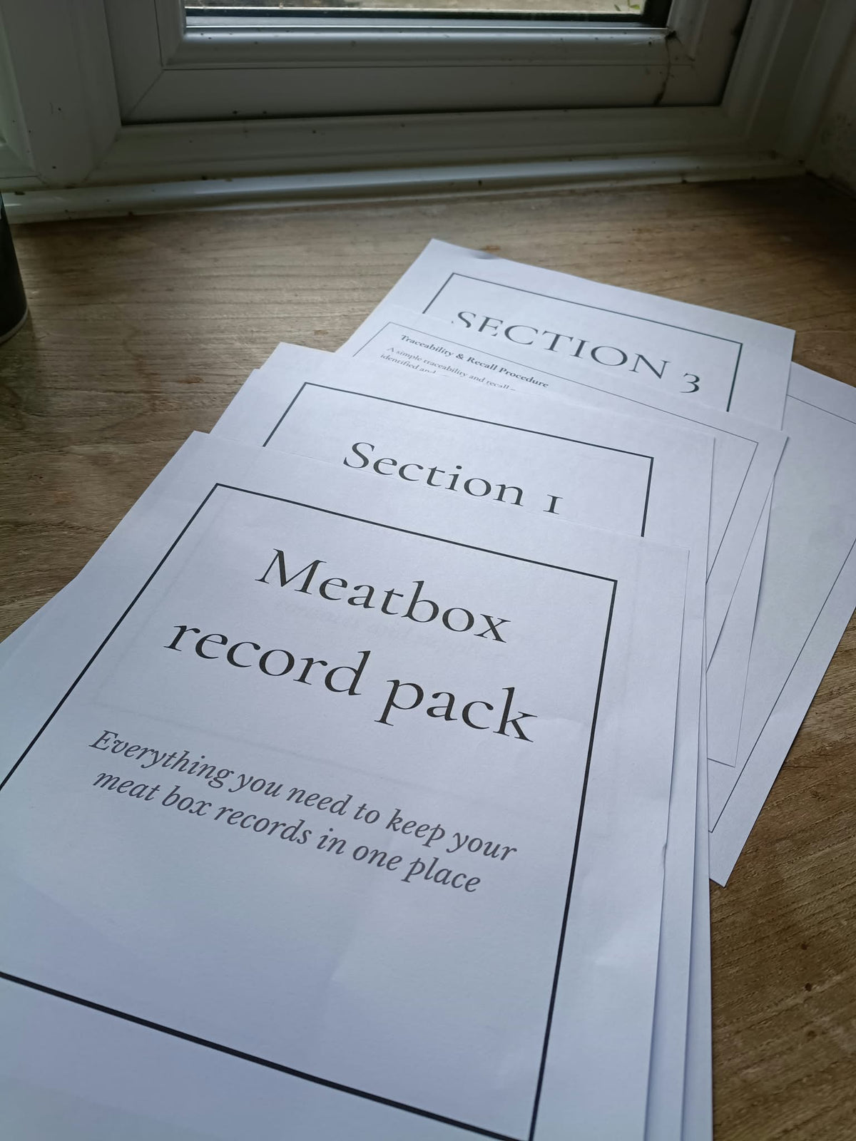 A stack of printed paper templates titled 'Meatbox record pack' and 'Section 1' resting on a wooden floor near a window.