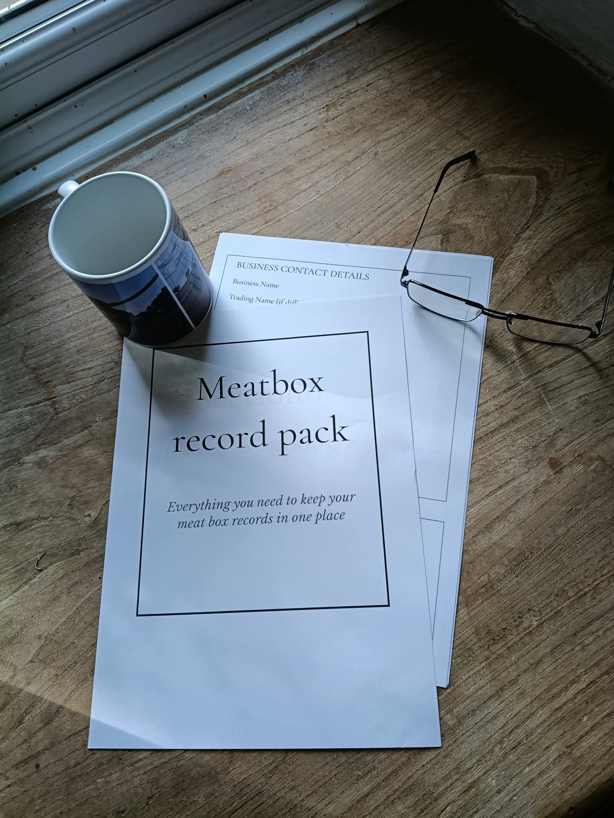 pages of the meatbox record pacl=k placed on a wooden windowsill, with a empty mug and a pair of glasses next to them.